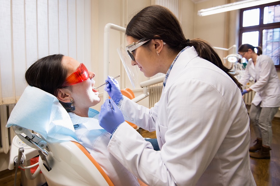 Zdjęcie przedstawia dwie uczennice kierunku higieniskta stomatolgiczna uczące sę wykonywania zabiegu w jamie ustnej. Jedna uczennica siedzi na fotelu dentystycznym, druga uczennica wykonuje zabieg przy użyciu narzędzi dentystycznych.