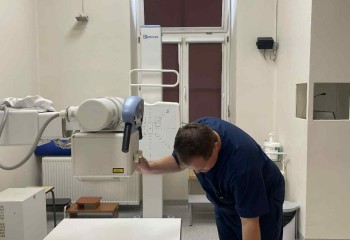 Zdjęcie przedstawia słuchacza wykonującego badanie diagnostyczne z zakresu elektrokardiologii. Widzimy aparat rentgenowski i dotykającego go słuchacza.