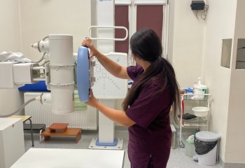 Zdjęcie przedstawia słuchacza wykonującego badanie diagnostyczne z zakresu elektrokardiologii. Widzimy aparat rentgenowski i dotykającego go słuchacza